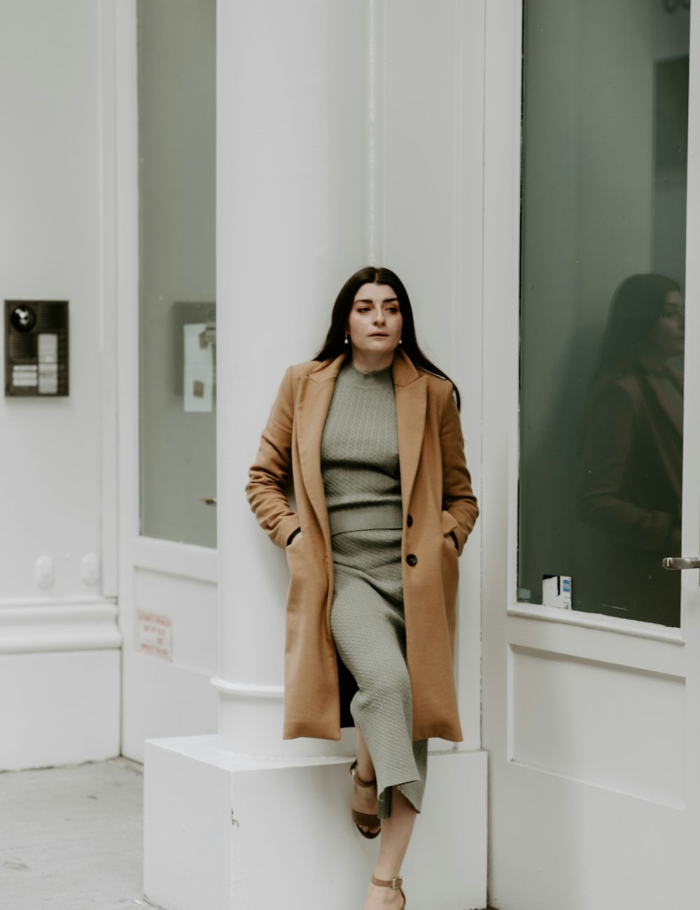 Una clienta con abrigo largo camel y vestido de punto frente a la vitrina de la tienda
